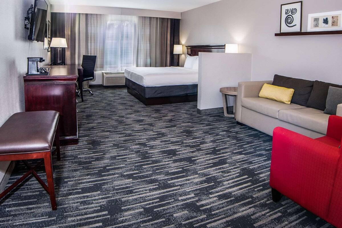 A hotel room with a bed, a desk, a chair, a sofa, a TV, and a coffee machine.