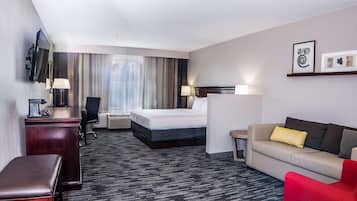 A hotel room with a bed, a desk, a chair, a sofa, a TV, and a coffee machine.