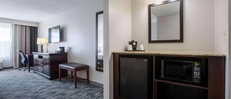 A hotel room with a desk, chair, and a minibar with a microwave.