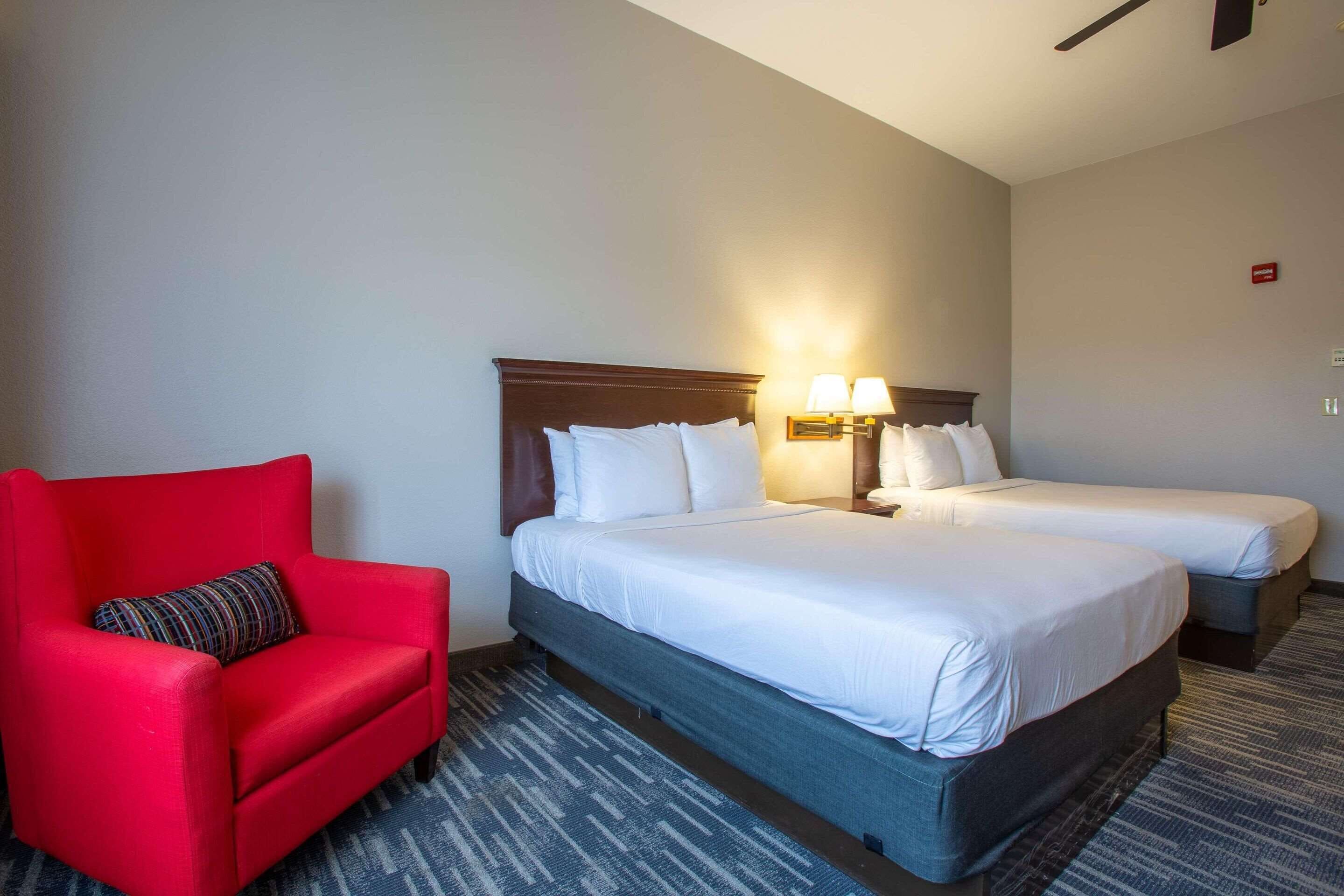 A hotel room with a large bed, two bedside tables with lamps, a red armchair, and a patterned rug.