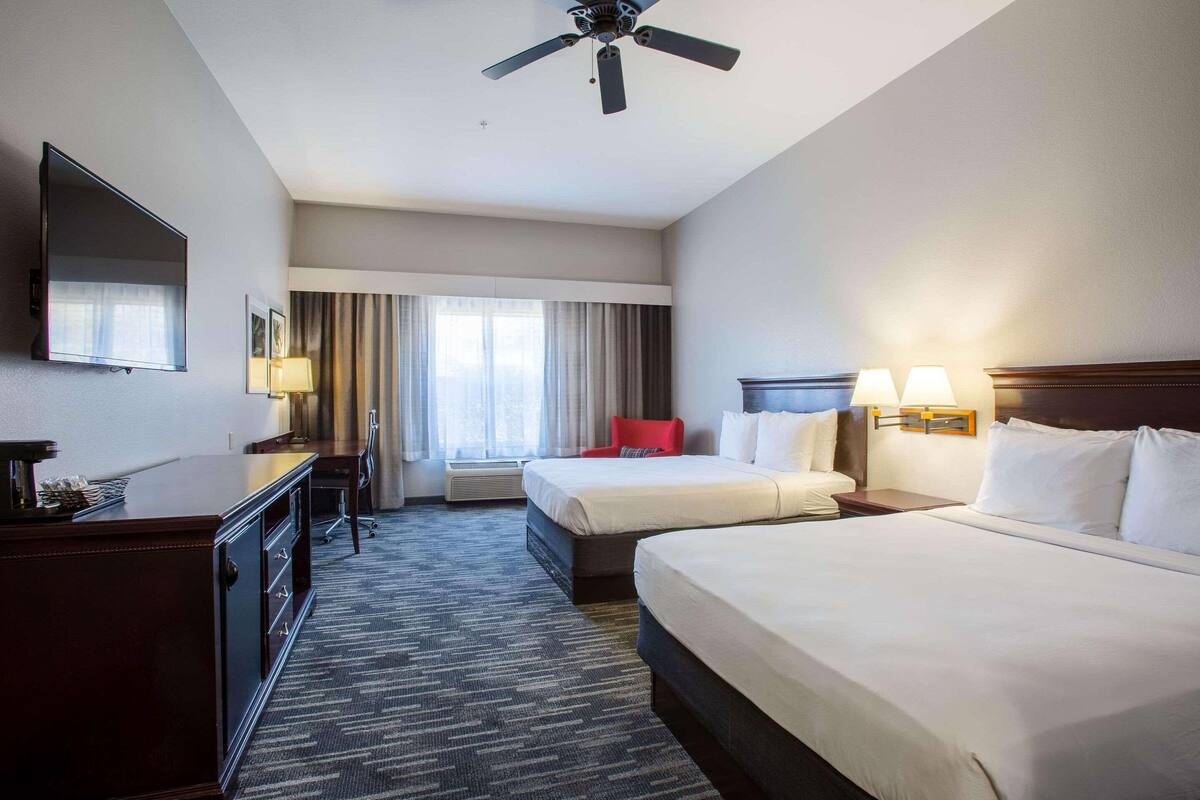 A hotel room with two beds, a desk, a TV, and a ceiling fan.