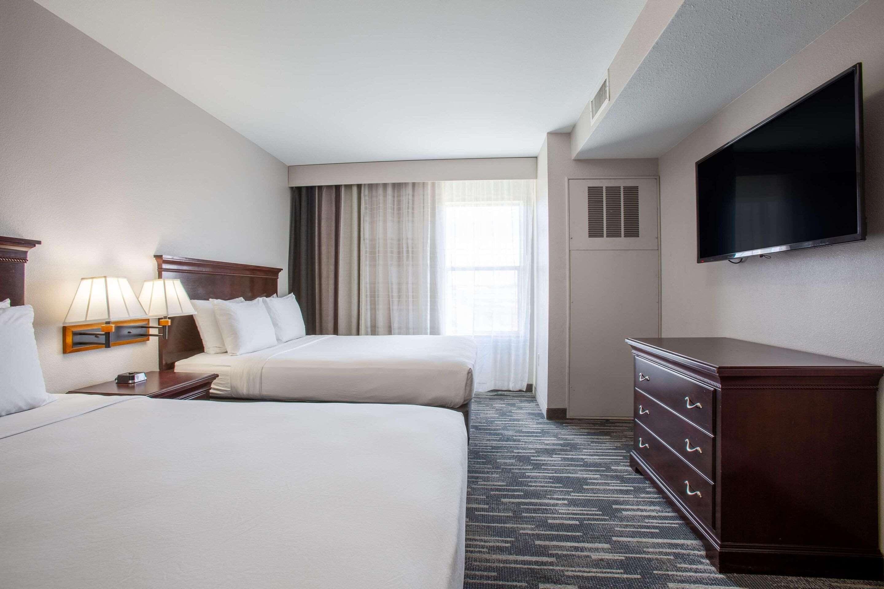 A hotel room with two beds, a dresser, a TV, and a window with curtains.