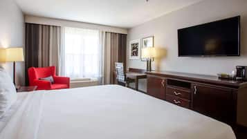 Ett hotellrum med en stor säng, ett skrivbord, en stol, en tv och ett fönster med gardiner.