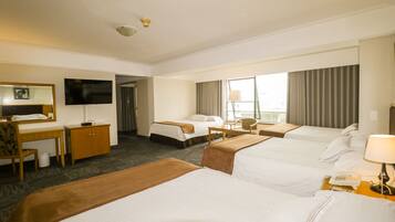 A hotel room with three beds, a desk, a chair, a TV, and a window with curtains.