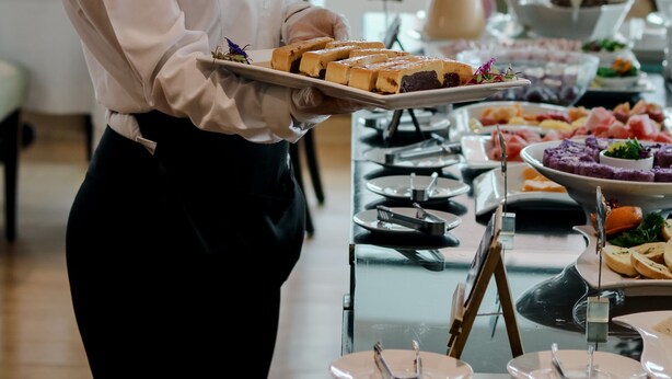 Un buffet proposant une variété de plats, avec un serveur vêtu d’une chemise blanche et d’un nœud papillon noir.