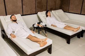 Dos sillones reclinables para masaje en un spa, con una bandeja de refrescos en el centro.
