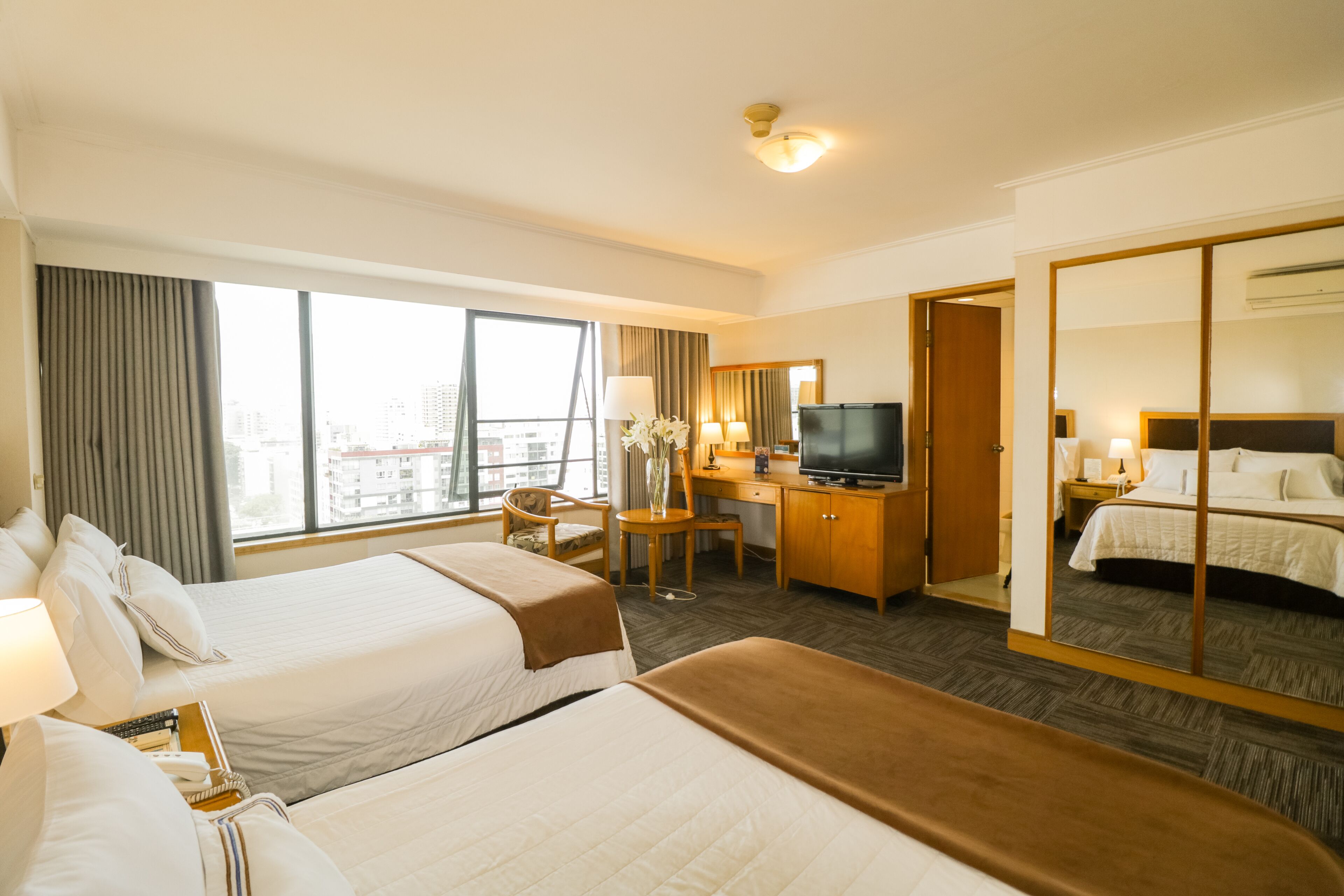 A hotel room with two beds, a desk, a television, and a large mirror.