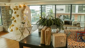 Un intérieur moderne avec un espace d’accueil agrémenté d’une arche de ballons, d’une plante en pot et d ’une table où sont disposés des sacs-cadeaux et des cadeaux emballés.