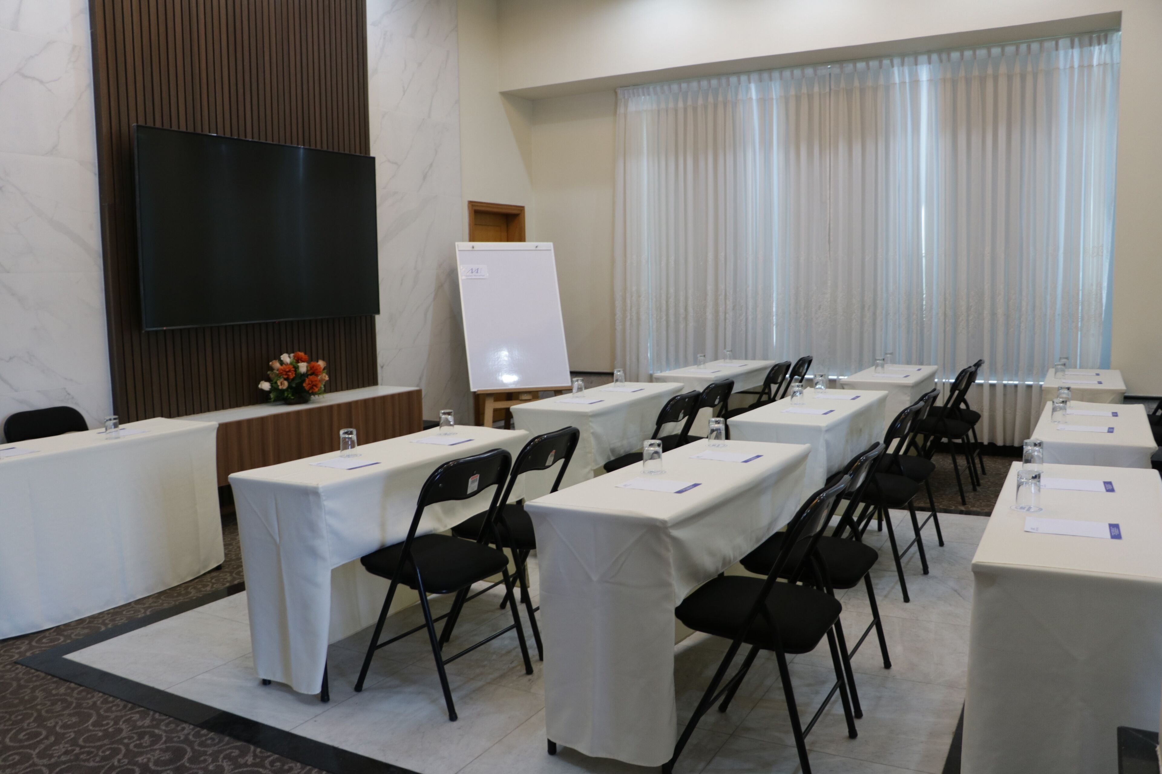 A conference room with long tables, chairs, a whiteboard, and a TV screen.