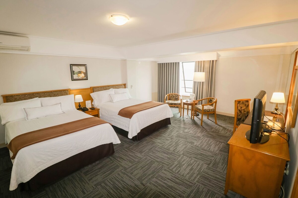 A hotel room with two beds, a desk, a chair, a television, and a window with curtains.