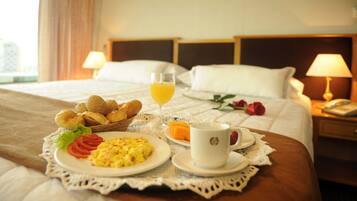 Una cama impecable con una bandeja de desayuno que incluye croissants, huevos revueltos y un vaso de jugo de naranja.