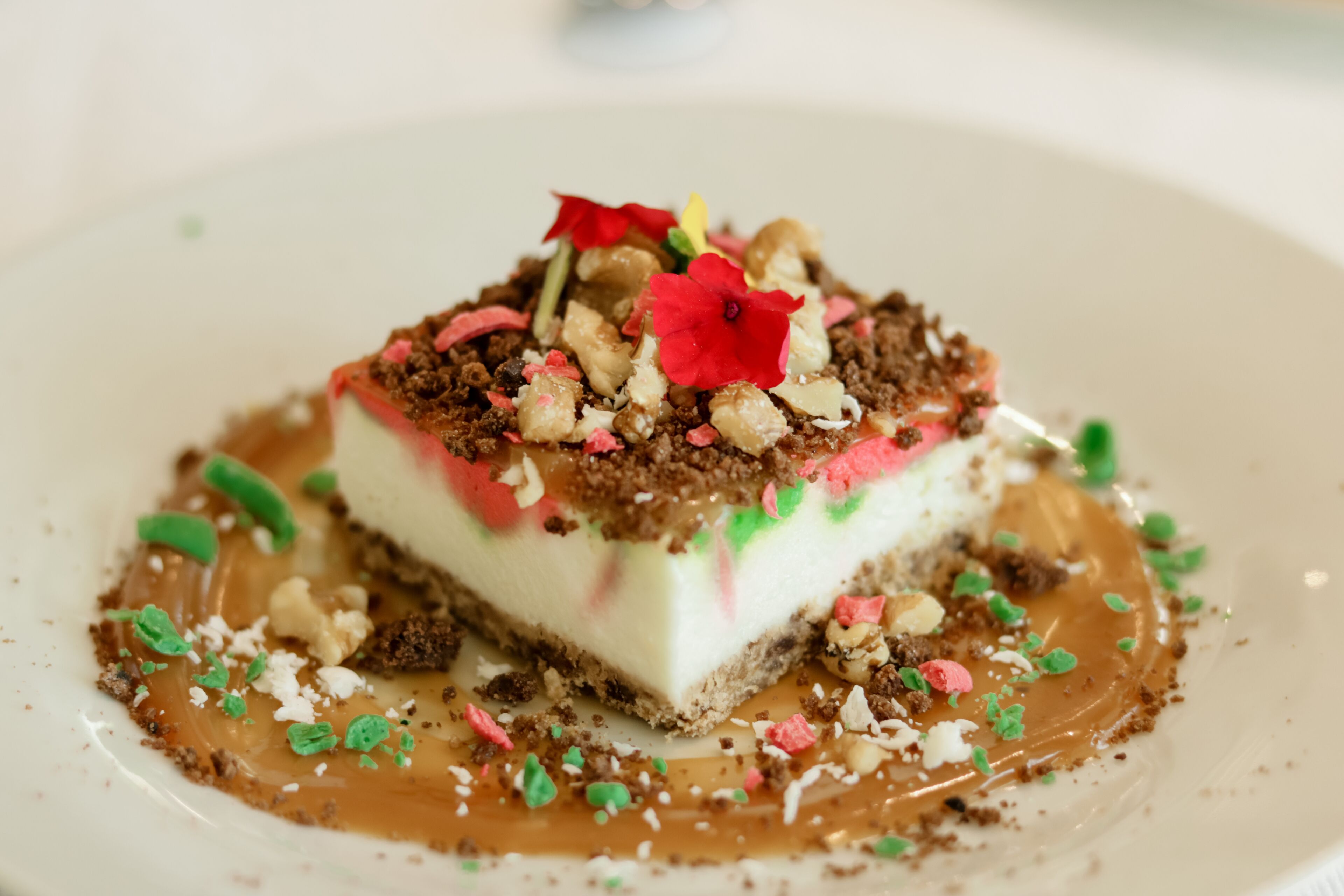 A dessert with a layered structure, topped with colorful sprinkles and a flower, served on a white plate.