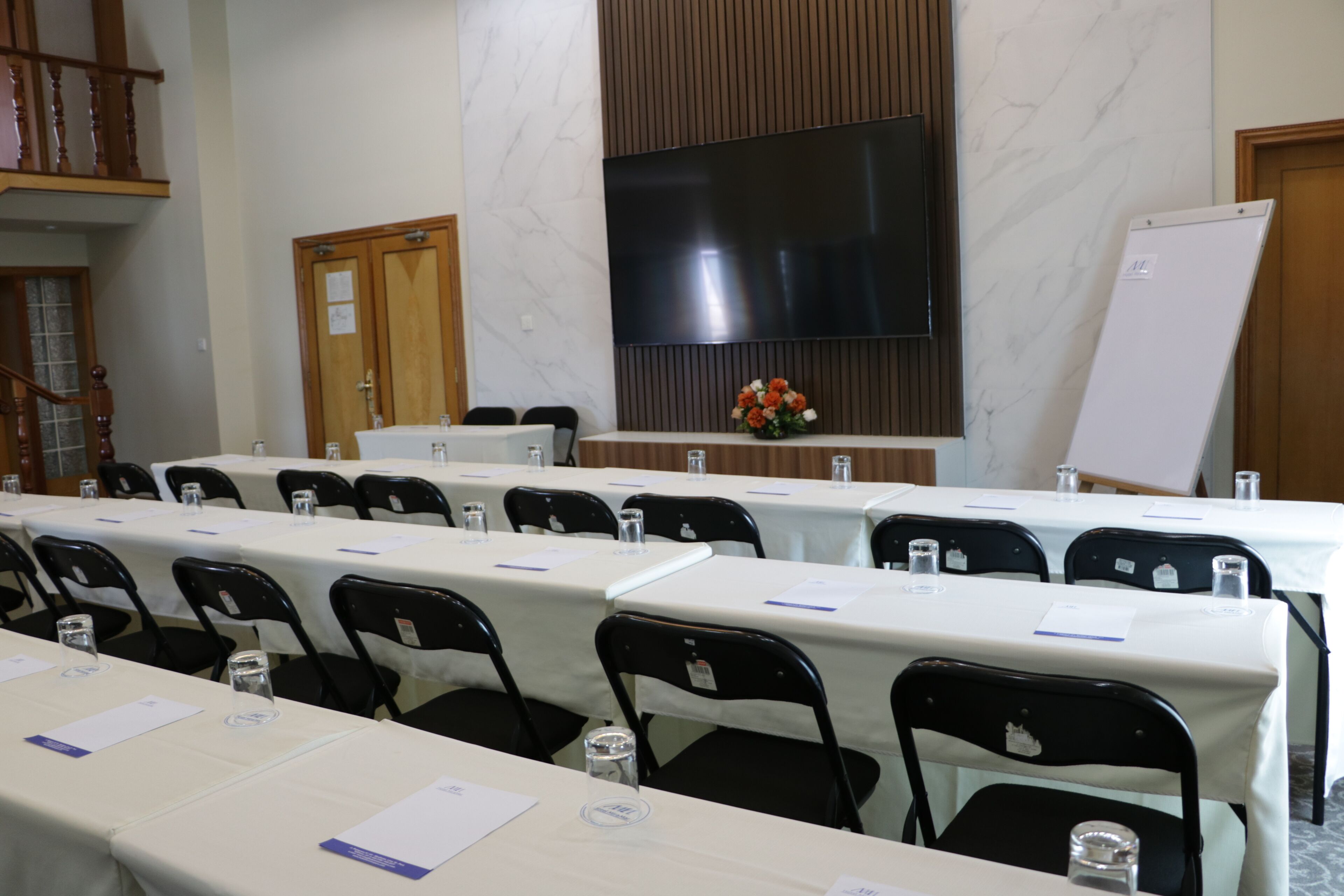 A conference room with multiple tables and chairs, a large flat-screen TV, and a whiteboard.