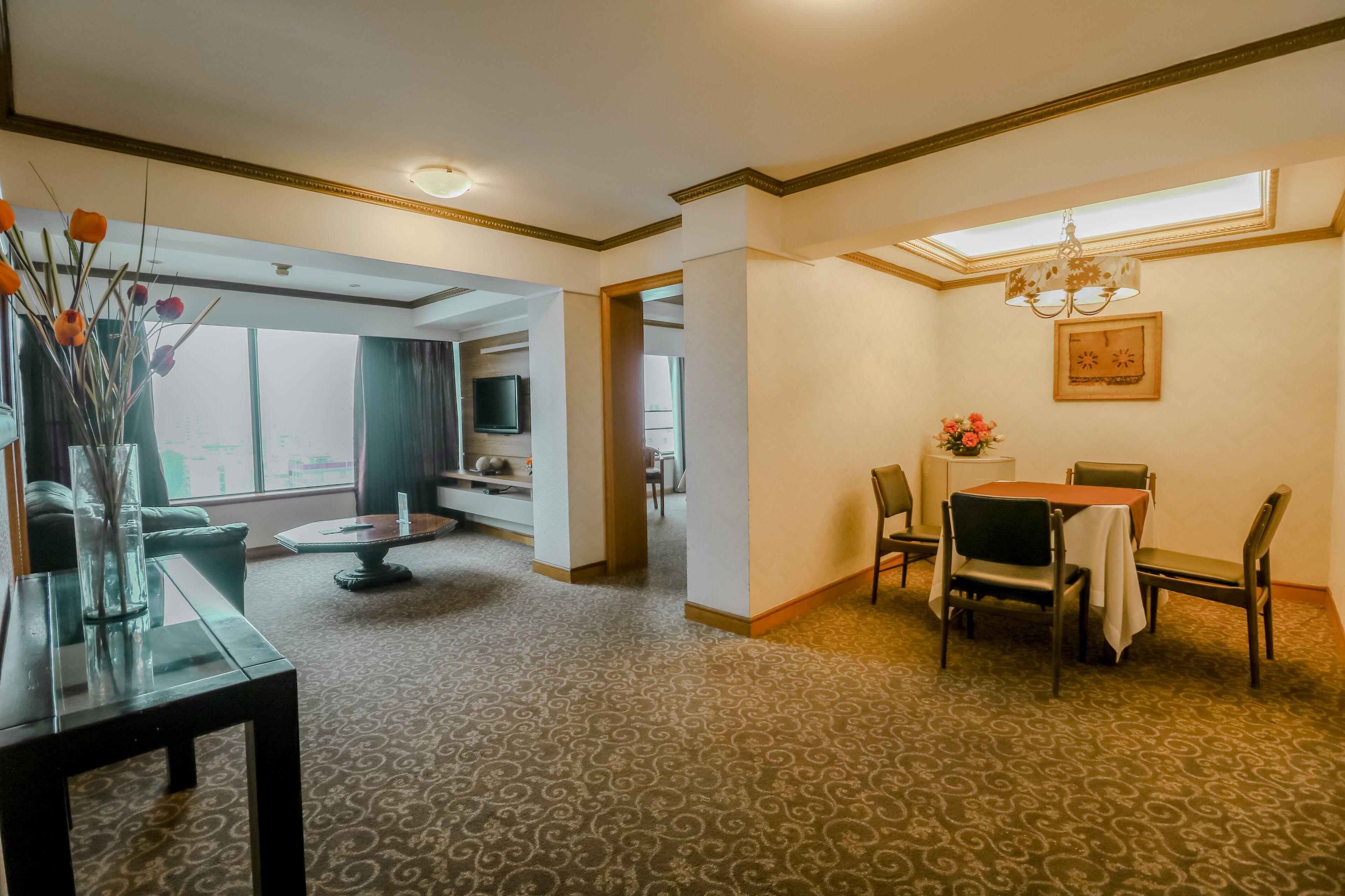 A hotel room with a dining area, a living room, and a view of the city.