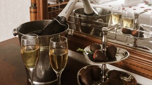 Une chambre d’hôtel avec un lit, une table de chevet sur laquelle se trouvent une bouteille de champagne, des verres et des fraises enrobées de chocolat.