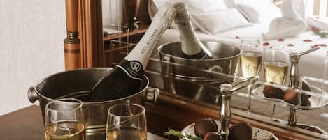Habitación de hotel con cama, mesita de noche, una botella de champán, copas y fresas cubiertas de chocolate.