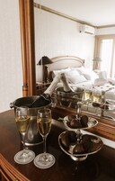 Habitación de hotel con cama, mesita de noche, una botella de champán, copas y fresas cubiertas de chocolate.