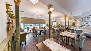 A restaurant with wooden tables, chairs, and ornate columns. - Capital Plaza Hotel (Bucharest)
