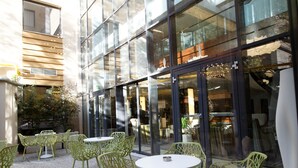 An outdoor seating area with green chairs and tables, large glass windows, and a building facade. - Capital Plaza Hotel (Bucharest)