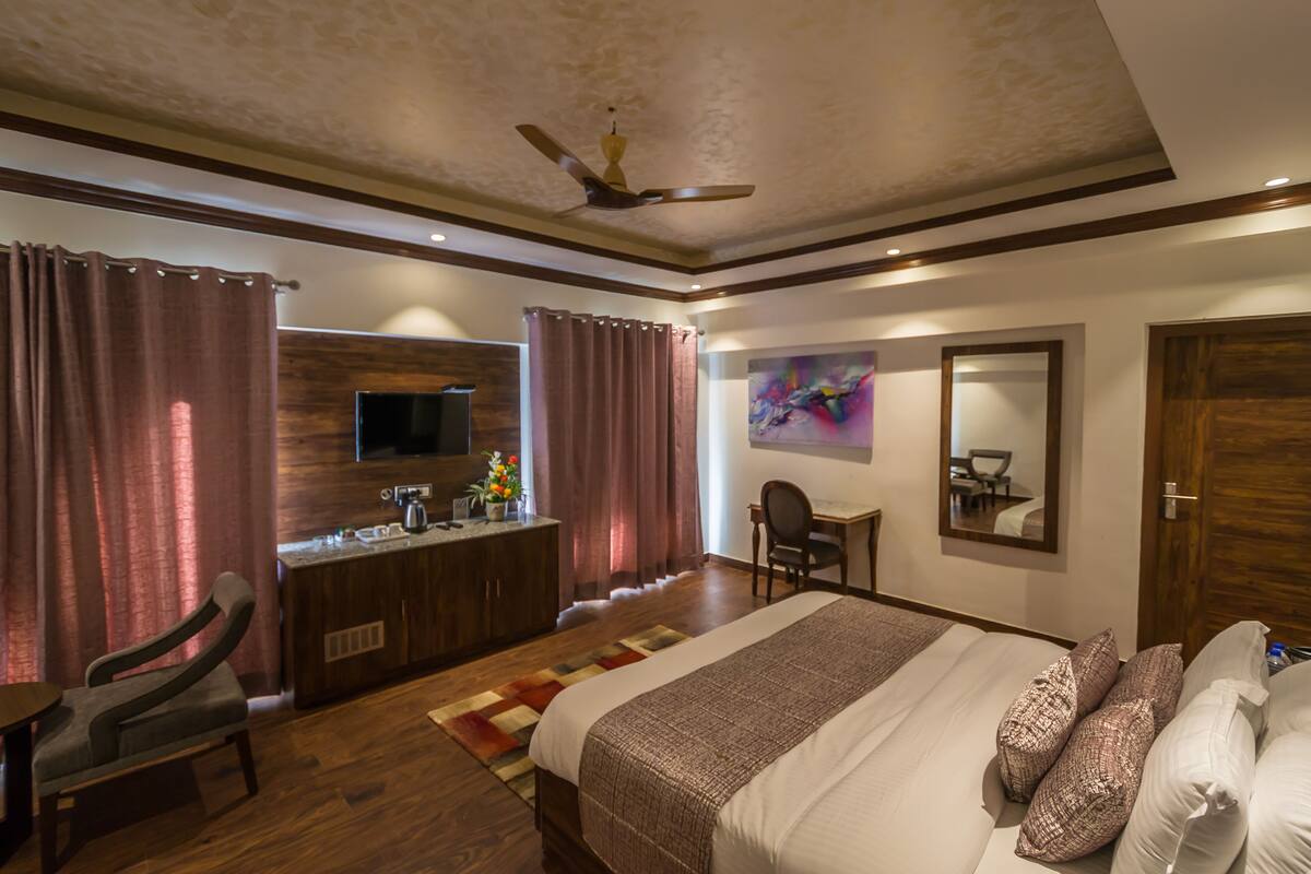 A hotel room with a bed, a desk, a chair, a television, and a ceiling fan.