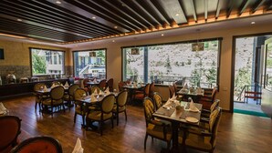 Ein Restaurant mit Holzböden, gedeckten Tischen mit weißen Servietten und großen Fenstern mit Blick auf ein Gebäude und Bäume.