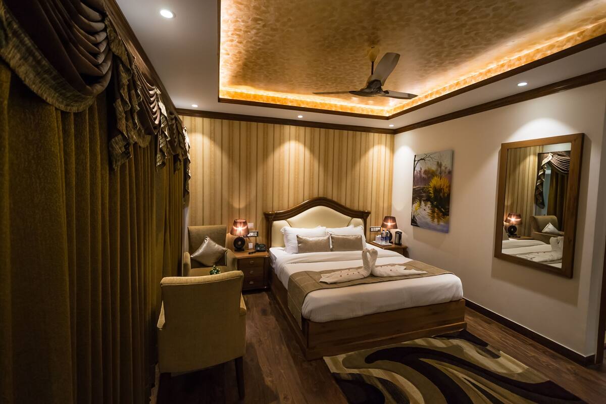 A hotel room with a large bed, a sitting area, a ceiling fan, and a painting on the wall.