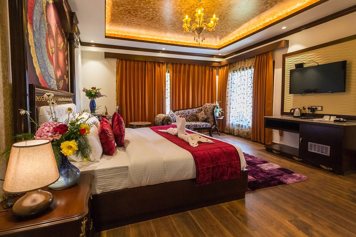A spacious bedroom with a large bed, a TV, a desk, and a chandelier.