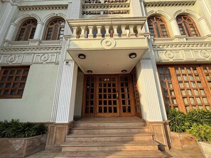 A grand entrance with a wooden door, steps leading up to it, and a balcony above. - Hotel Pradeep (Varanasi)