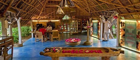 A traditional wooden structure with a thatched roof, a reception desk, and a welcome sign.