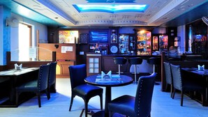 Eine Bar mit Tischen und Stühlen, eine Theke mit Speisekarte und eine Decke mit dekorativer Beleuchtung.