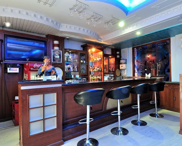 Una zona de bar con barra, taburetes y una pantalla de televisión.