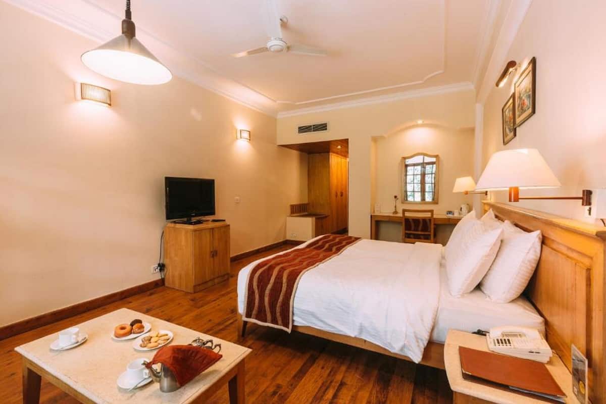 Ein Hotelzimmer mit Bett, Nachttisch, Lampe, Fernseher und einem kleinen Tisch mit Frühstücksgebäck.