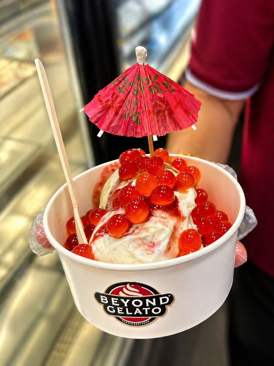A cup of ice cream with red fruit toppings and a small umbrella, labeled 'Beyond Gelato.'