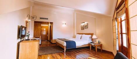 A hotel room with a bed, bedside table, lamp, and a dining area with a table set for breakfast.