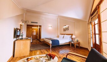 A hotel room with a bed, bedside table, lamp, and a dining area with a table set for breakfast.