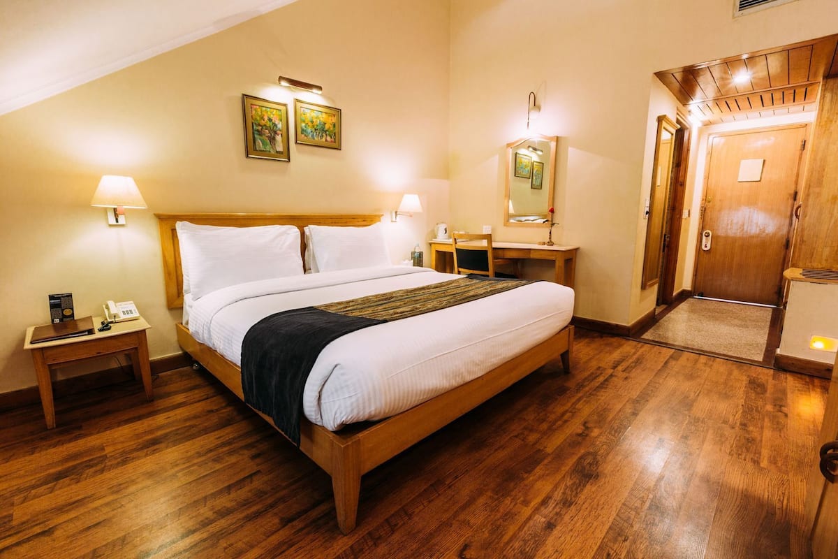 Ein Hotelzimmer mit einem hölzernen Bett, Nachttischlampen, einem Schreibtisch, einem Spiegel und einer Tür.