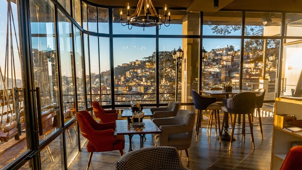 A modern interior with large windows, a chandelier, and a view of a hillside cityscape. - Hotel Willow Banks, Mall Road Shimla (Shimla)