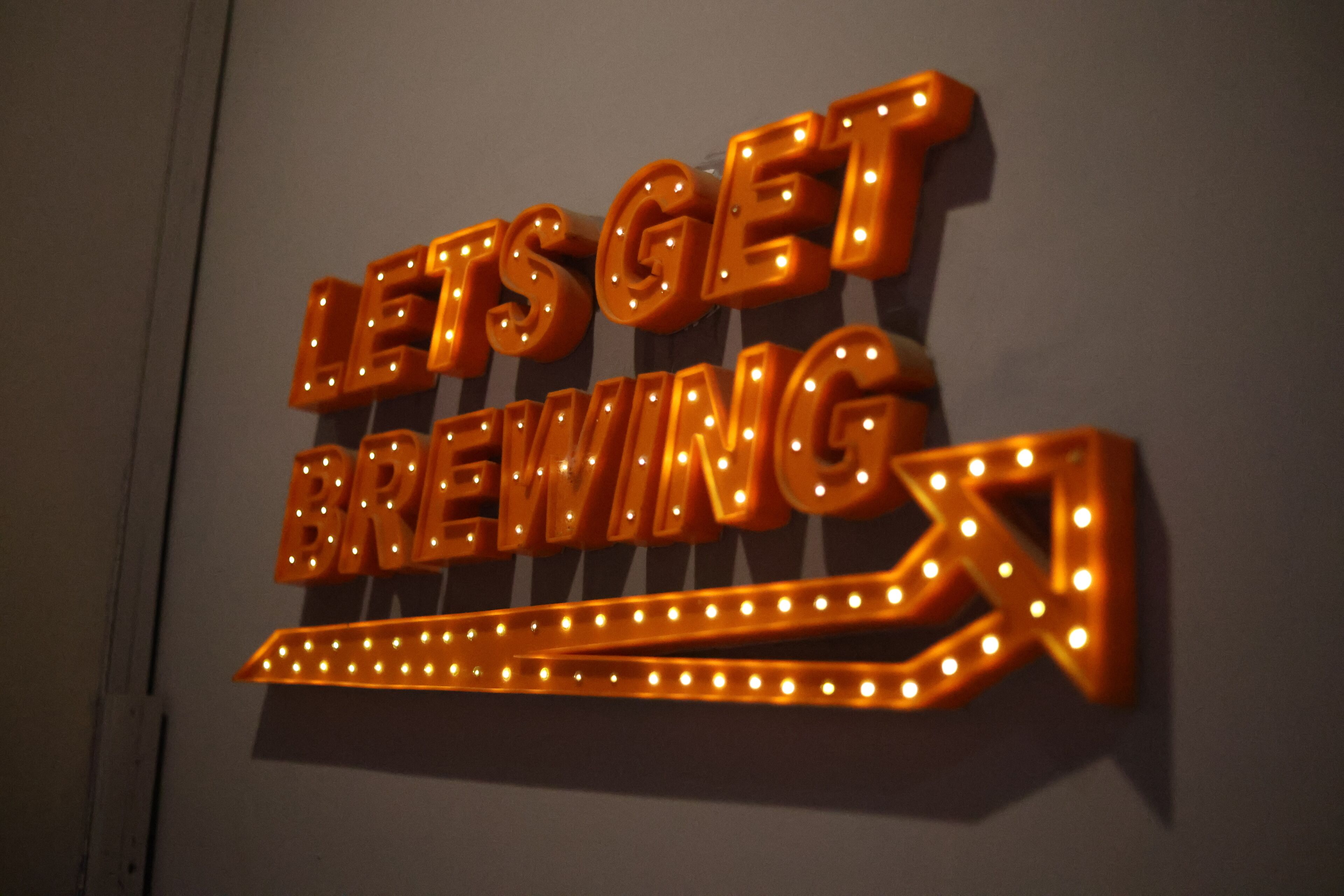 Un letrero de neón con el texto "LET'S GET BREWING" sobre un fondo oscuro.