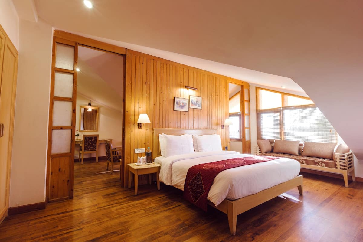 Ein Schlafzimmer mit Holzboden, einem Bett mit weißer Bettwäsche, einer hölzernen Bank und einem Fenster mit Jalousien.