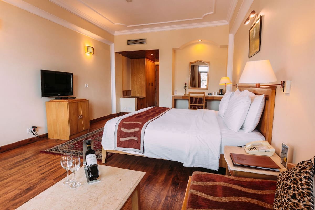 Ein Hotelzimmer mit Bett, Schreibtisch, Fernseher, Lampe, Telefon und einer Weinflasche.