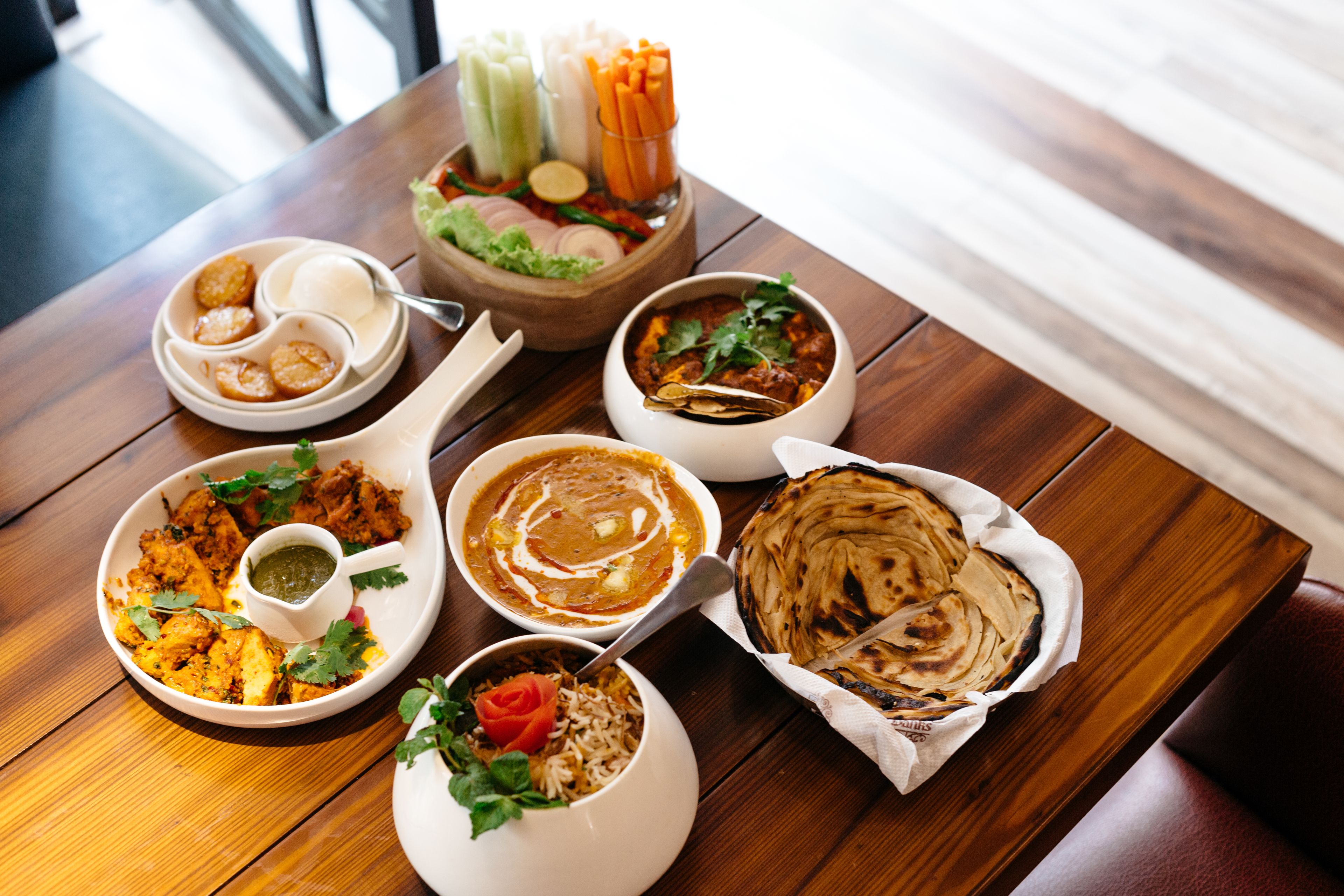 A wooden table with various dishes including naan bread, curry, and rice.