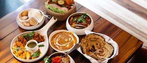 A wooden table with various dishes including naan bread, curry, and rice.