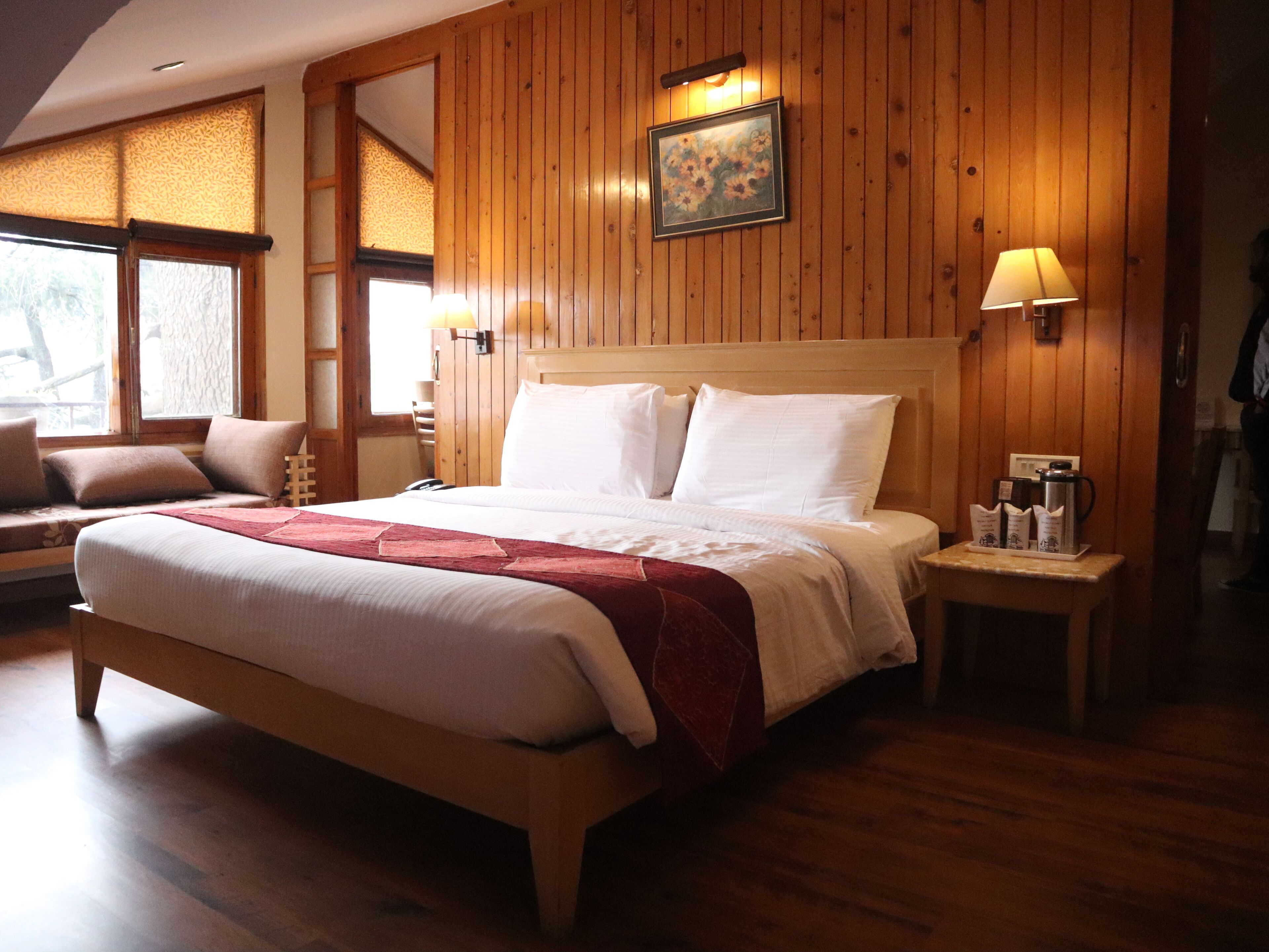 A wooden-paneled room with a bed, a nightstand, a lamp, and a painting on the wall.