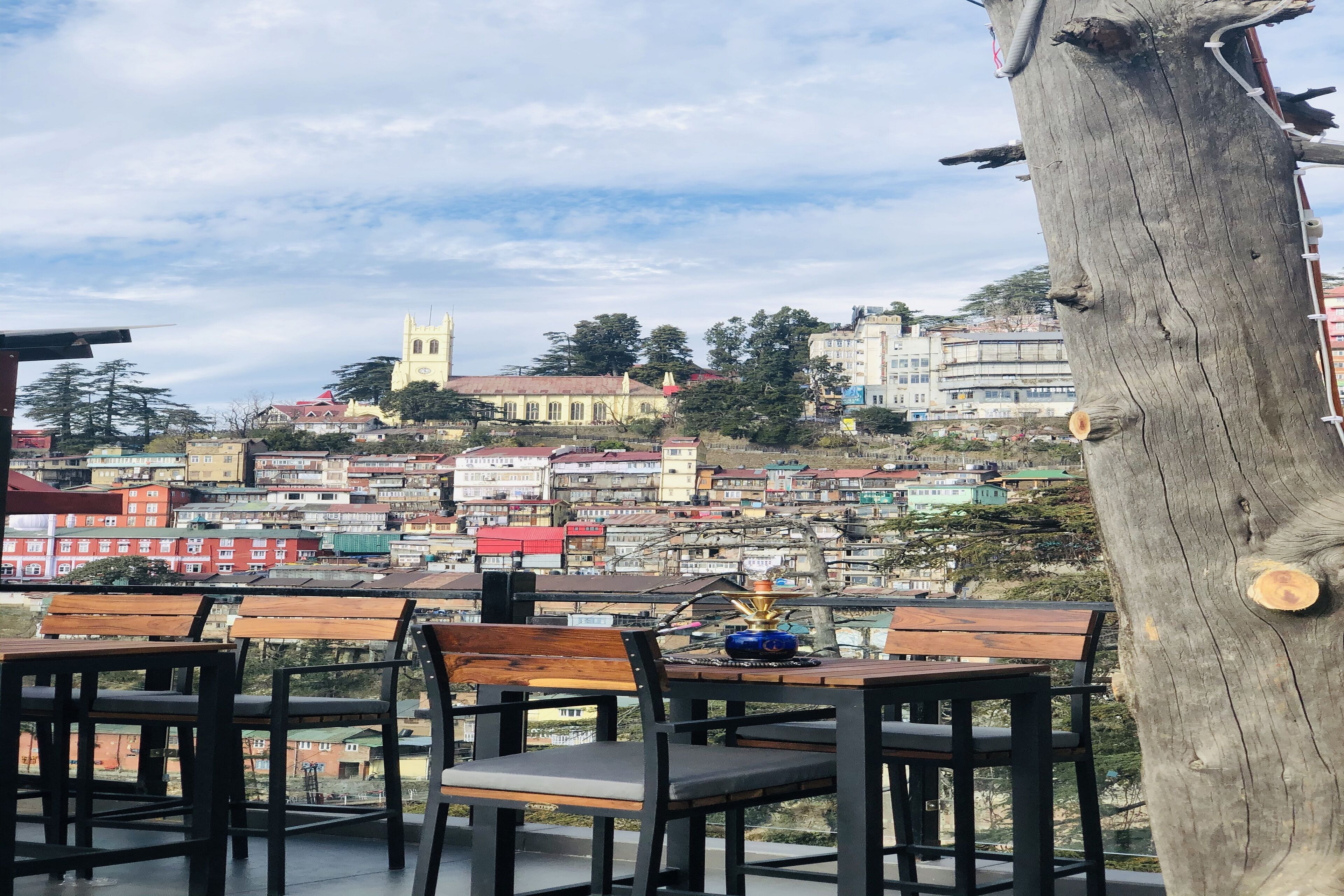 Una terraza con muebles de madera y vistas a un paisaje urbano con edificios y una iglesia.