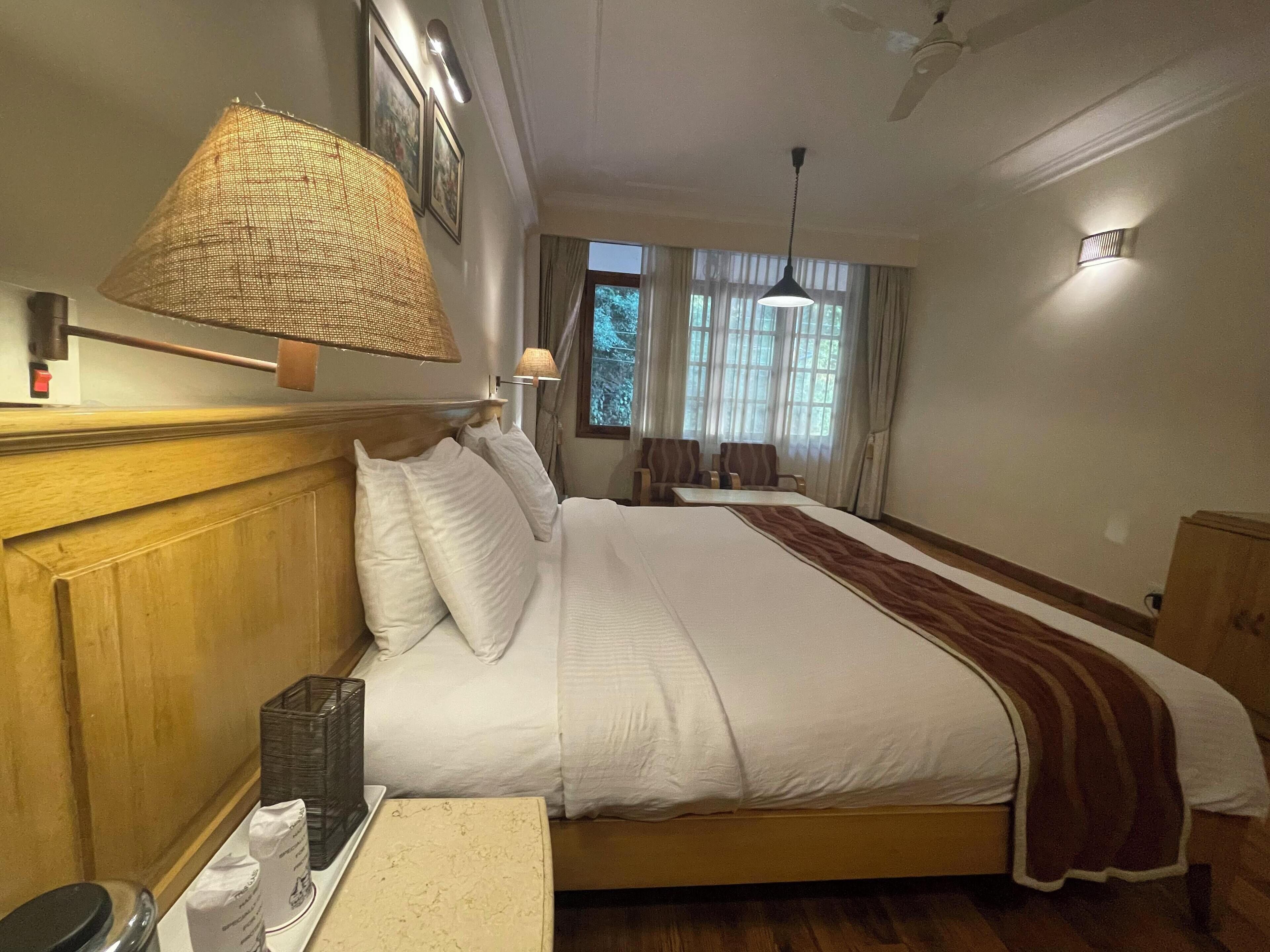 A hotel room with a large bed, a bedside table, a lamp, and a window with curtains.