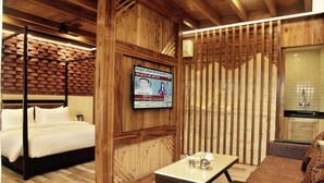 A wooden-themed room with a bed, a table with a cup and saucer, and a television mounted on the wall. - Hotel Willow Banks, Mall Road Shimla (Shimla)