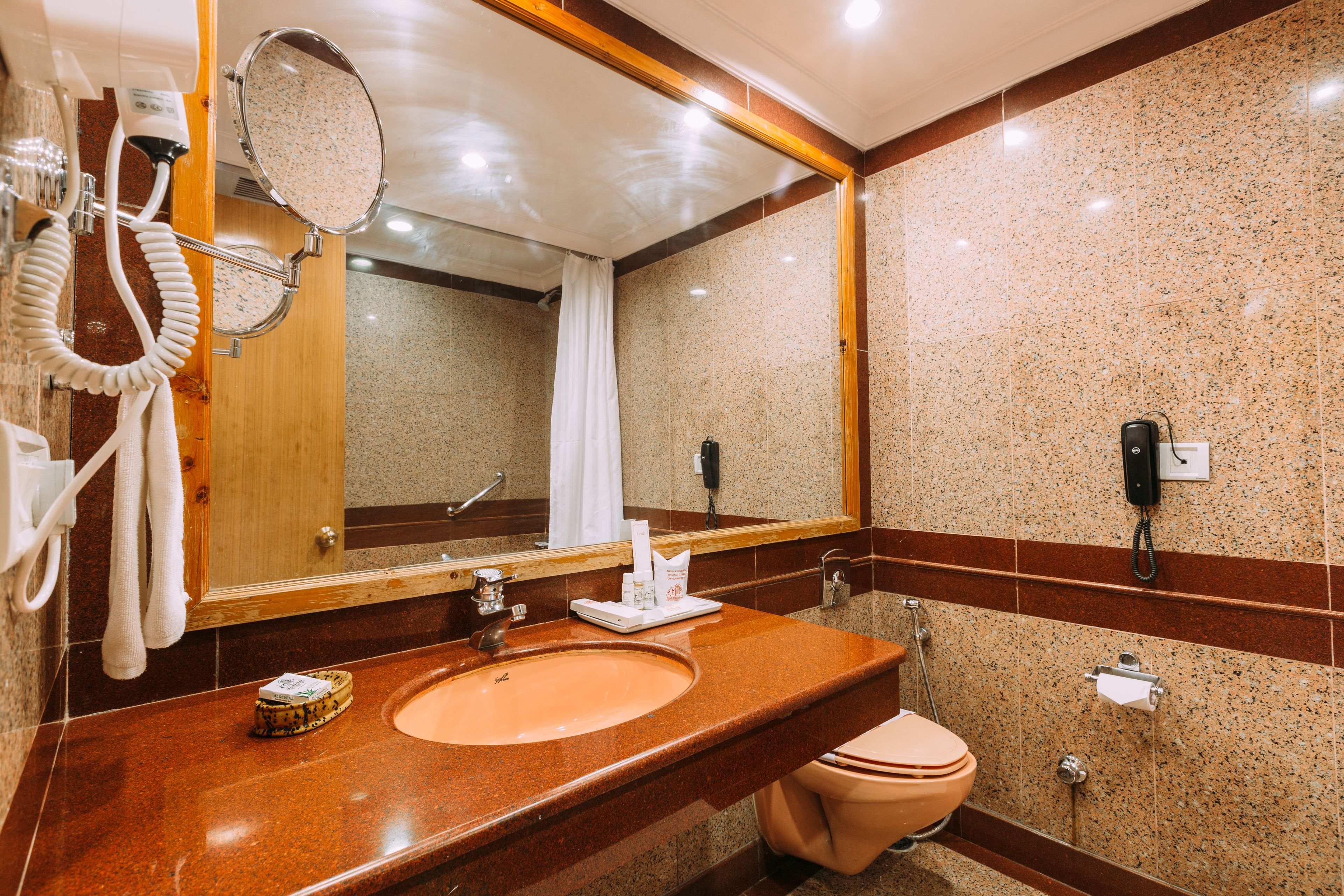 A bathroom with a granite countertop sink, a mirror, a hairdryer, and a toilet.