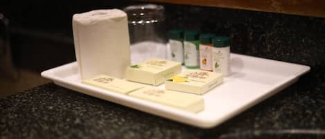 A white rectangular tray on a dark countertop with a roll of toilet paper, several bars of soap, and two bottles of lotion.