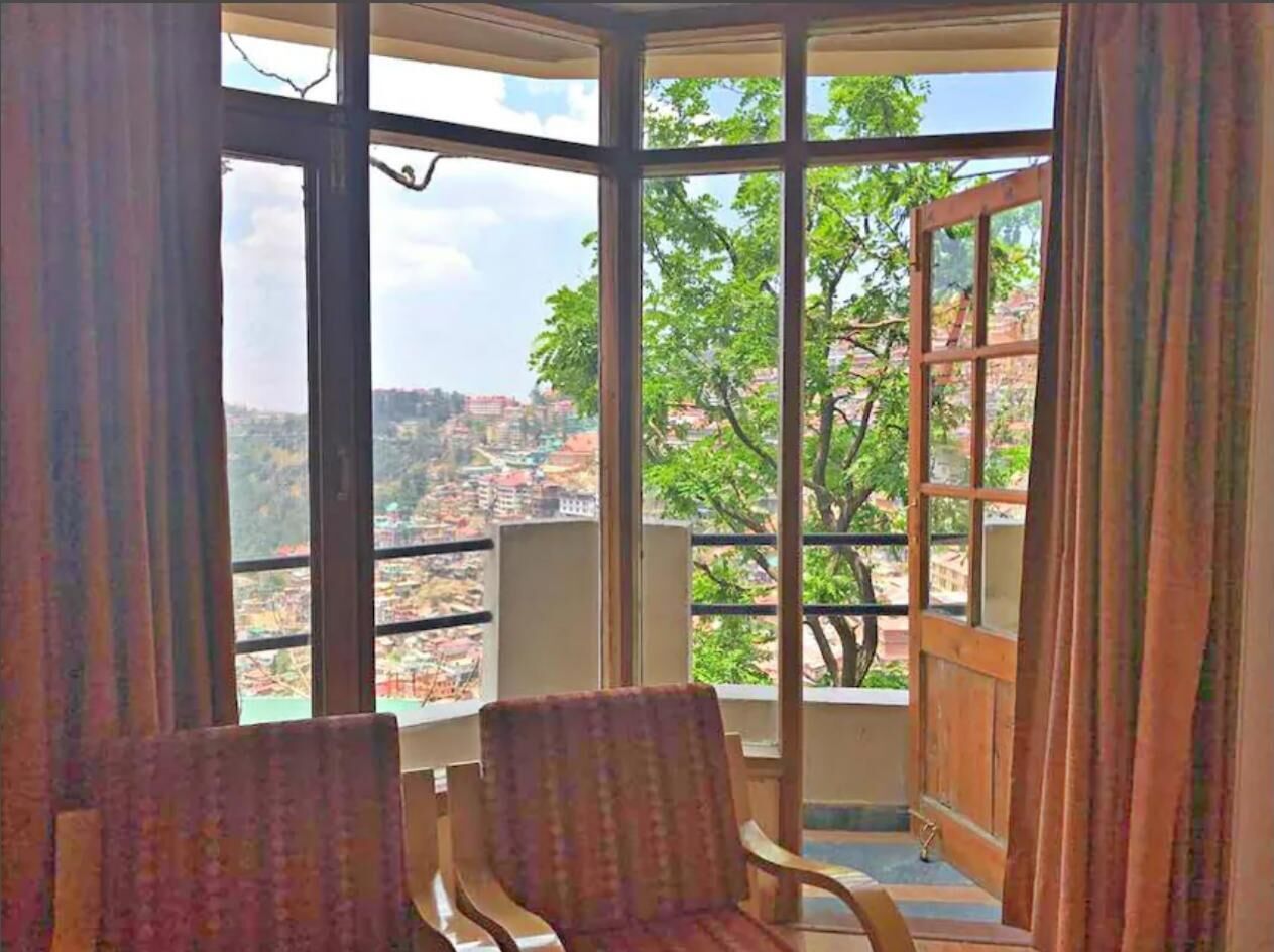 Una habitación con un ventanal grande, dos sillas y vistas a un paisaje urbano.
