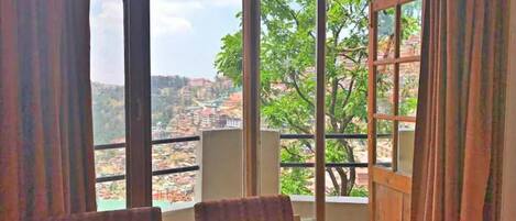 Una habitación con un ventanal grande, dos sillas y vistas a un paisaje urbano.